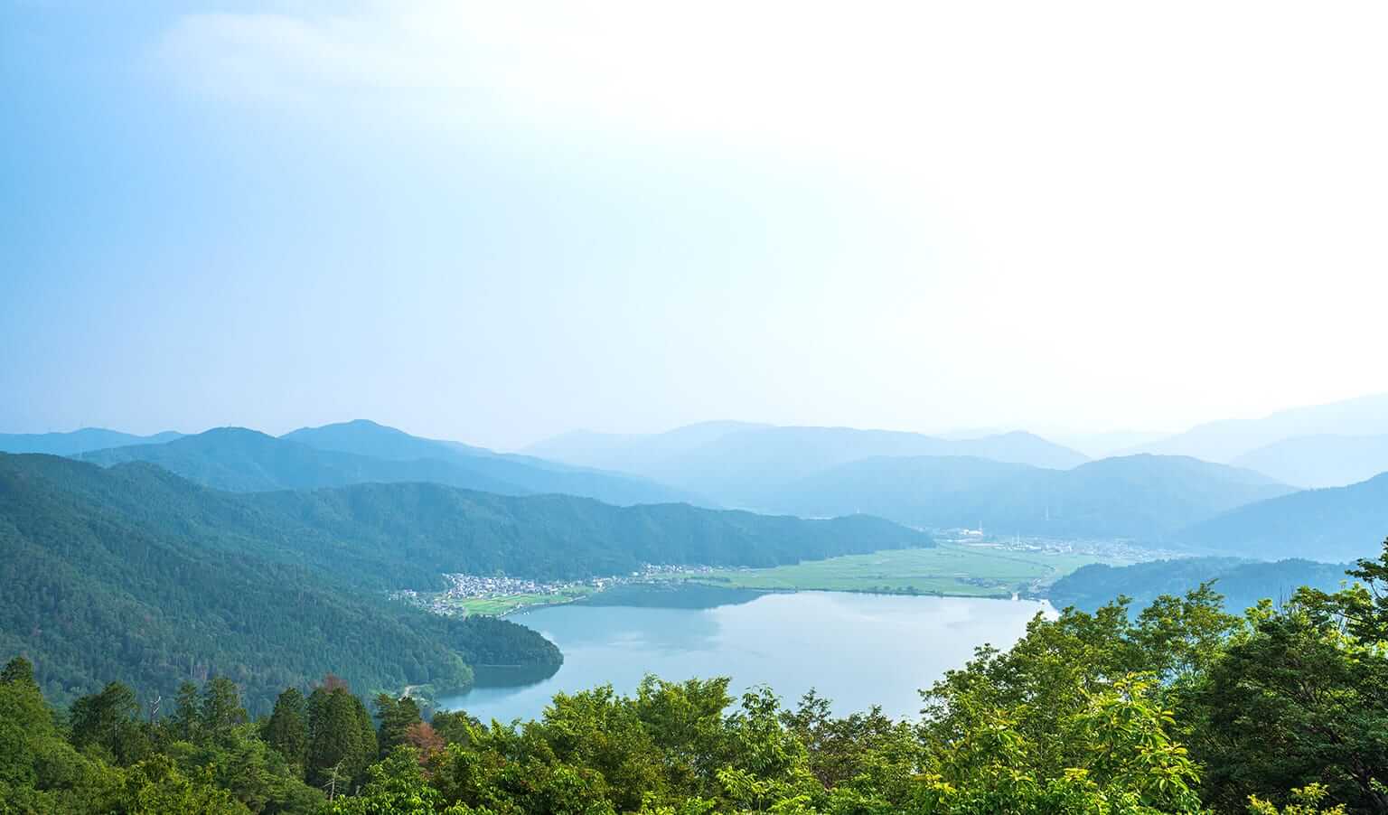 賤ヶ岳の山並みと湖。手前に緑が広がり、奥には青空と穏やかな水面が見える。静かで落ち着いた雰囲気